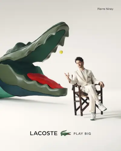 En smart vision i et råhvidt jakkesæt, Pierre Niney står foran Lacoste Play Big-reklamen.