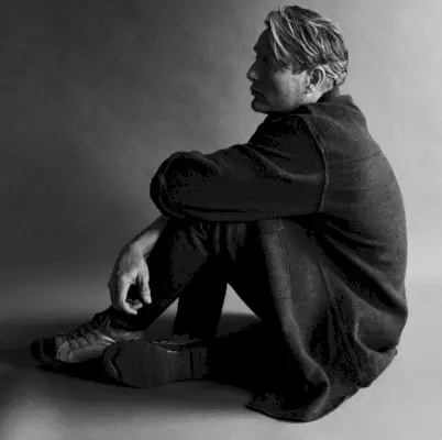 Apărând într-o fotografie alb-negru, Mads Mikkelsen poartă o cămașă Raey cu A.P.C. blugi.