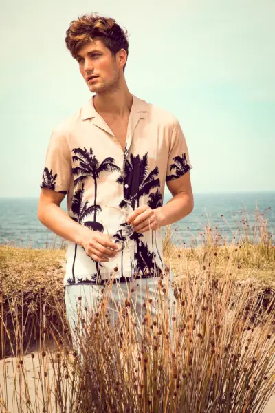 Adoptant une ambiance estivale, Saxon porte une chemise à imprimé palmiers à col camp Zara avec un pantalon.