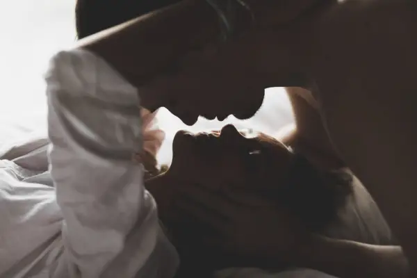 Couple in partial silhouette, faces close to each other anticipating a kiss home bedroom on white linens.