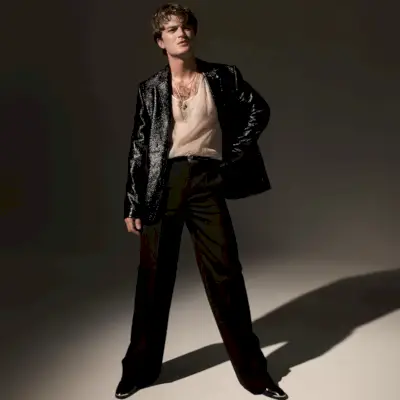 Joe Keery sfoggia un blazer Courrèges con pantaloni Valentino, una canotta Dior Men e stivali Celine.