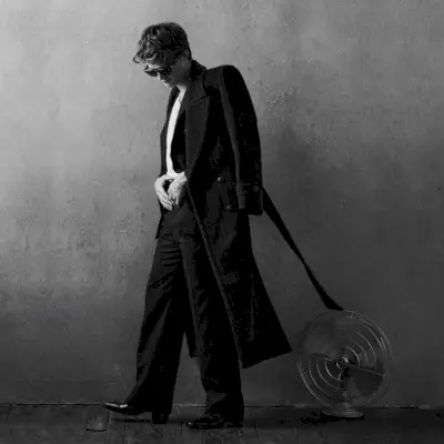 Una visione sartoriale, Joe Keery indossa un cappotto, un blazer e pantaloni Saint Laurent con una t-shirt Second/Layer, stivali Bally, occhiali da sole Akoni e un orologio Audemars Piguet.