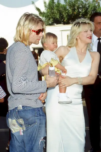 Kurt Cobain, Frances Bean Cobain și Courtney Love participă la MTV Video Music Awards din 1993. Kurt poartă un tricou în dungi cu mânecă lungă, blugi din denim învechiți și ochelari de soare roșii.