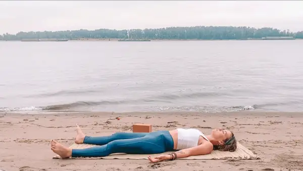 Woman lying on her back on a yoga mat in Savasana beneath the full Moon in Pisces