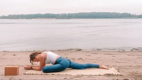 Woman lying on her belly with one knee bent and the other leg straight in Sleeping Swan, a Yin Yoga pose