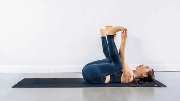 Kassandra Reinhardt lying on her back on a yoga mat practicing Happy Baby Pose while doing Yin Yoga for the new Moon