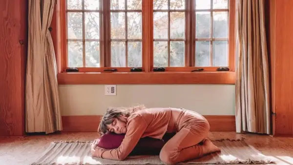 Woman practicing Yin Yoga by draping herself onto a bolster or pillow with her knees and forearms on the yoga mat