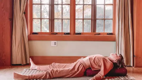 Woman lying on a yoga mat doing Yin Yoga in Supported Savasana