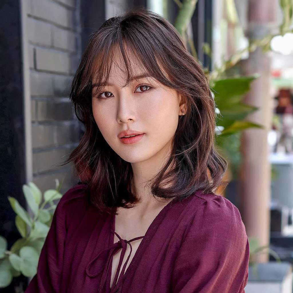 שיער ברונטית גלי באורך בינוני עם פוני וילון רך הממסגר את הפנים ויוצר מראה טבעי לחיות' title=