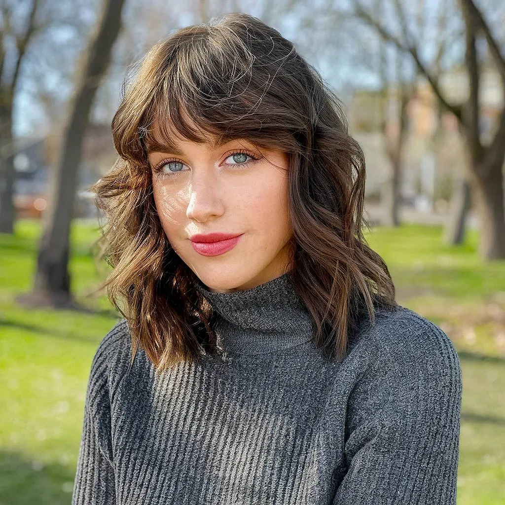 שיער גלי במרקם עד הכתפיים עם פוני צמרמורת וגוונים ברונטיים טבעיים לסגנון רך ללא מאמץ' title=