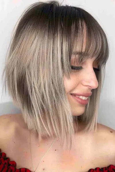 Woman with a tapered blonde bob and long bangs showing dark to light color gradient