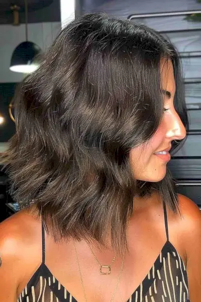 Side view of a woman with a long choppy inverted bob in deep brown