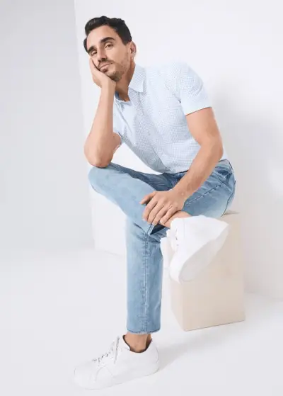 Vrhunski model Arthur Kulkov nosi potiskano srajco s kratkimi rokavi in ​​denim kavbojke znamke Van Heusen.