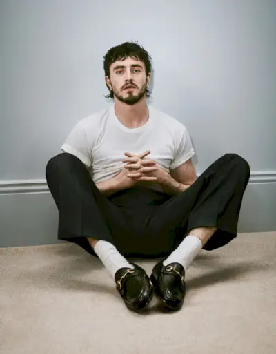 Daļēji ikdienišķs baltā T-kreklā un biksēs Pols Meskāls ir Gucci Horsebit 1953. gada loafer kampaņas seja.