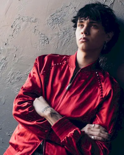 Landon Barker가 Valentino의 빨간색 새틴 보머 재킷을 입고 사진을 위해 포즈를 취하고 있습니다.