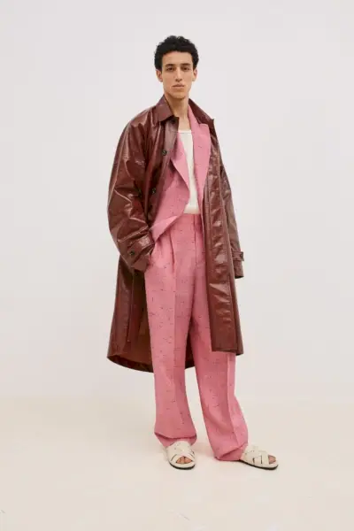 Walid Fiher presenta un look contemporaneo di Bottega Veneta, abbinando un trench lucido color sangue di bue a un abito rosa strutturato, completato da sandali color crema minimalisti.