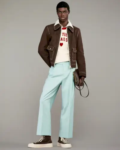 Zaram Obasi decupează o siluetă izbitoare într-o jachetă de piele intoarsă Harry Lambert for Zara Cutie Chaos și pantaloni albaștri de gheață, completate de o cămașă cu guler și un tricou grafic.