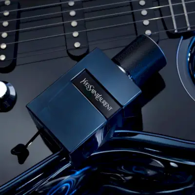 魅惑的なフレグランスの広告では、洗練されたイヴ・サンローラン Y エリクサーのボトルが主役となり、光沢のあるギターの上に置かれています。