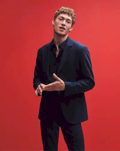 Valentin Humbroich sticker ut med karismatisk lätthet mot en slående röd bakgrund, och har på sig en skräddarsydd marinblå Calvin Klein-kostym.