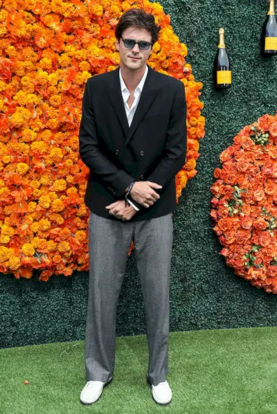 Jacob Elordi vnáší do Veuve Clicquot Polo Classic klasický hollywoodský šarm, kombinuje výrazné dvouřadé černé sako s uvolněnými šedými kalhotami, kompenzované ležérními bílými mokasíny, a dotváří vzhled nadčasovými slunečními brýlemi – perfektní spojení tradičního krejčovství a uvolněnosti. elegance.