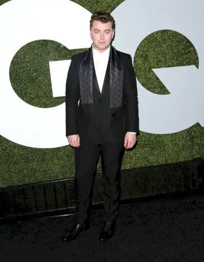 Sam Smith indossa uno smoking marsigliese a un bottone con revers a lancia in raso nero Gucci con una camicia bianca, una sciarpa di raso nero e stivali di pelle nera.