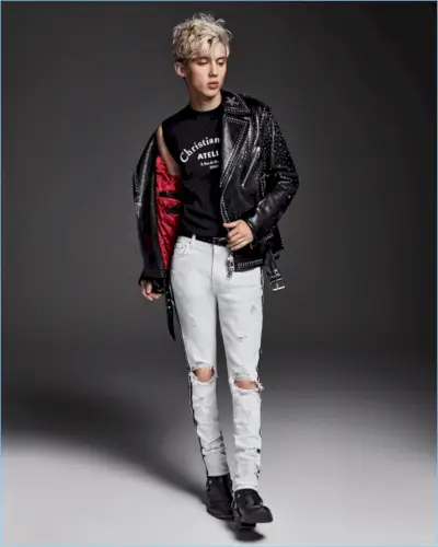 Uma visão cool, Troye Sivan veste um suéter Dior Homme sem mangas com uma jaqueta de couro Valentino. Ele também arrasa com jeans Amiri e botas Saint Laurent.