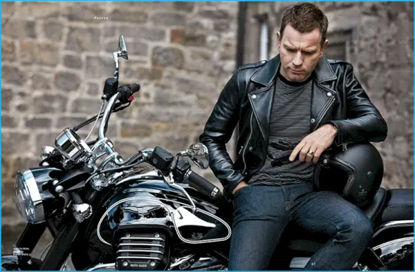 Ewan McGregor posa en una motocicleta, luciendo una chaqueta de motociclista de cuero de Tom Ford, jeans de Acne Studios y guantes Fratelli Orsini con una camiseta a rayas de Saint Laurent.