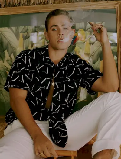 Dacre Montgomery rookt een sigaar en draagt ​​een AMIRI-shirt met een Ralph Lauren-broek.