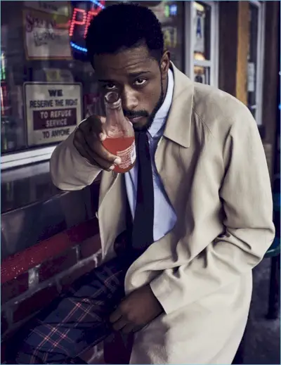 Desfrutando de uma bebida, Lakeith Stanfield veste um casaco Bottega Veneta com camisa e gravata Margaret Howell. Ele também arrasa com calças xadrez Louis Vuitton.