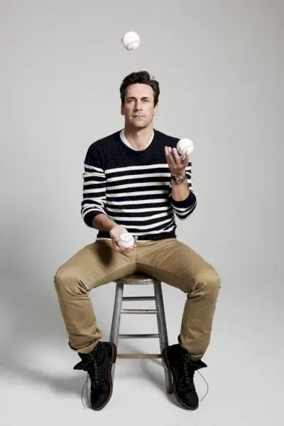 캐주얼한 스웨터와 치노룩을 입은 Jon Hamm은 야구공을 저글링합니다.