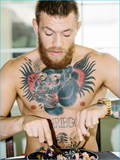 En Conor McGregor uten overkropp viser frem sine karakteristiske tatoveringer og graver seg inn i et måltid.