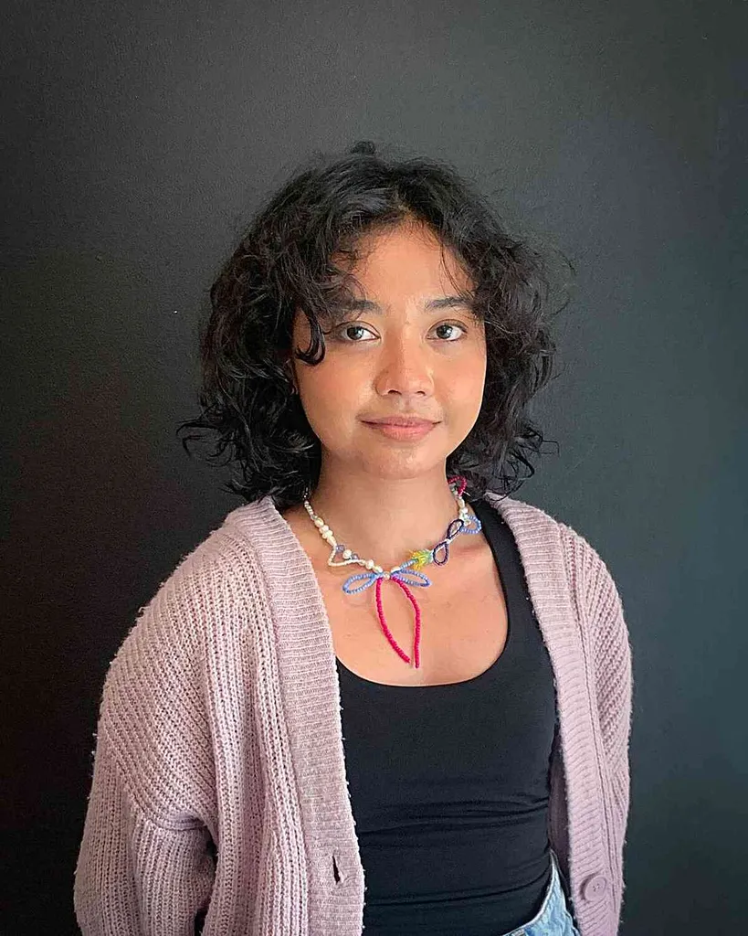 얼굴을 감싸는 커튼 앞머리가 있는 어깨 길이의 곱슬 밥' title=