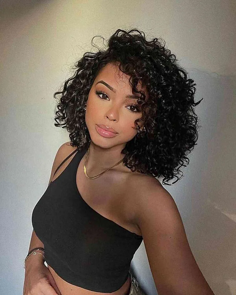 אישה בגזרת Cadō הכוללת שיער מתולתל קצר וחלק צדדי עמוק המעניקים סגנון דרמטי ונפחי' title=