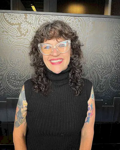 Medium-Length Curled Shag and Bangs for Women Wearing Glasses in Their Sixties