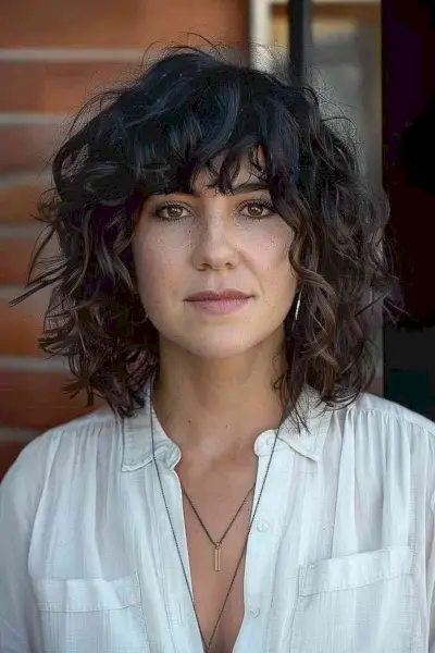 Curly shag hairstyle with textured bangs and layered cut for medium to thick curly hair.