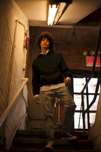 Liam usa moletom com capuz Alternative Apparel, camisa Gosha Rubchinskiy, jeans Dries Van Noten e tênis Converse.