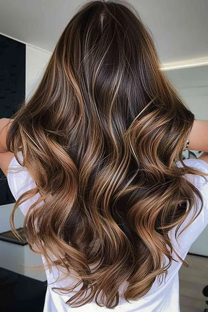 Cabelo longo e ondulado com destaques parciais de balayage de chocolate e caramelo' title=