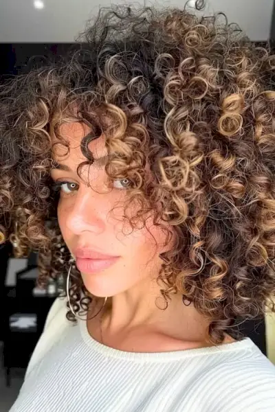 Karamelově blond odlesky na upnutých kudrnatých tmavě hnědých vlasech.