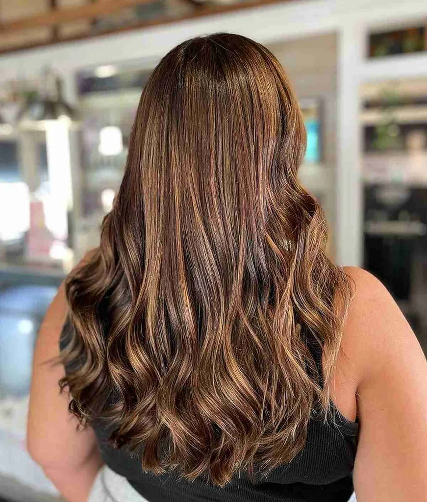 Karamelbalayage op bruin haar met gekrulde uiteinden' title=