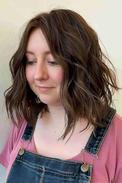 Medium-length tousled hairstyle with a side part for adding volume to thin hair, ideal for women with round, full faces.