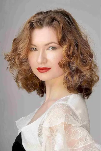 Medium length tapered curls with warm brown-blonde color, showcasing voluminous and playful texture.