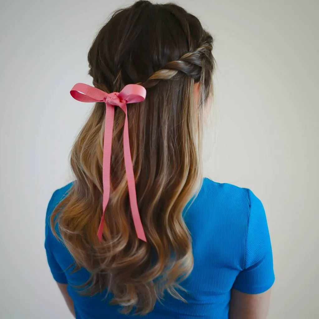 Peinado simple y retorcido hasta la mitad con acento de cinta rosa en cabello ondulado' title=