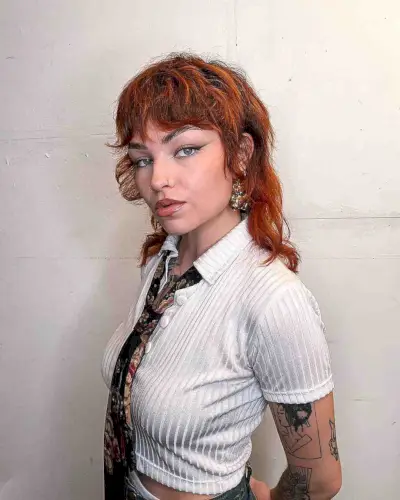 Fiery red shaggy mullet with micro bangs and layered texture on thick, wavy hair