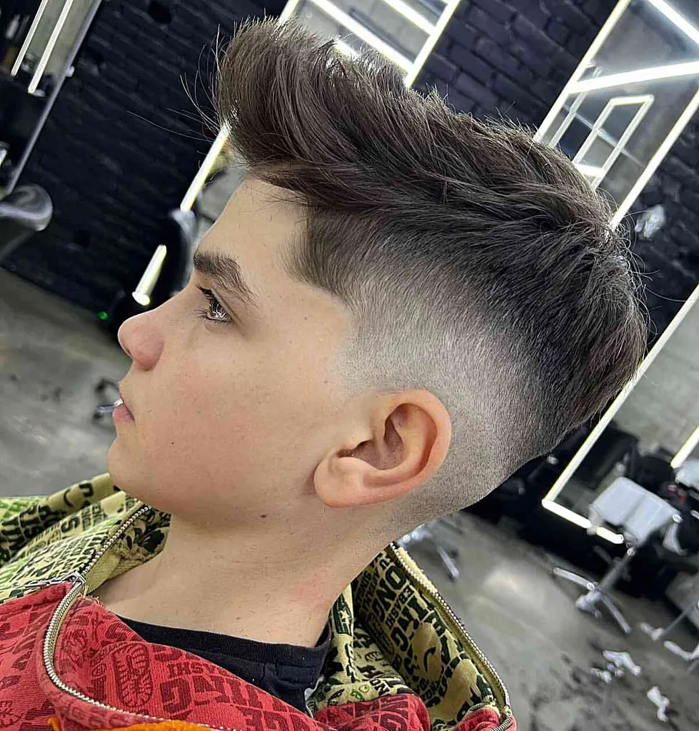 Mid Fade e Ciuffo per ragazzi con capelli lunghi sulla parte superiore e sui lati corti' title=