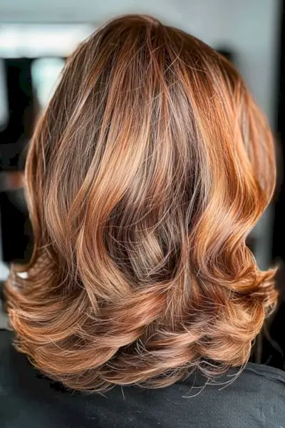 Subtile lagdelte bølger med kobberbalayage fremhæver mellemlang klipning.
