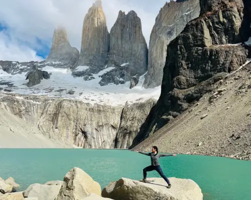 Ingrid Yang practicing yoga asana on a large rock in front of a green body of water. In the background are tall gray mountains, The Towers are located in Torres del Paine, the national park that is central to the Chilean side of Patagonia.
