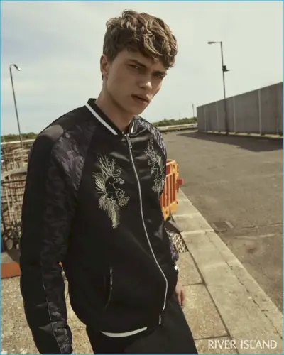 Jake Love poartă o jachetă bomber neagră din satin brodat de la River Island.
