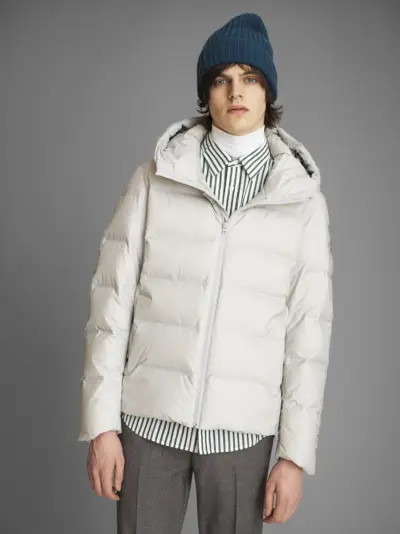 Alistair Waterfield luce una chaqueta de plumas con cuello alto, camisa a rayas y pantalones plisados ​​de UNIQLO.