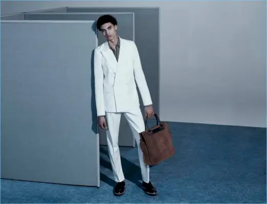 夏の白を取り入れたソル ゴスは、ドリス ヴァン ノッテンのダブルブレスト スーツにバレナ ベネチア ストライプのポロシャツを合わせています。ソルは、フェリージのオープントップ トート バッグとコモン プロジェクトのウェッジソール ダービーをアクセサリーにしています。