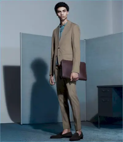 背の高いソル・ゴスは、P. ジョンソンのスーツにオーリーのニットポロ、チフォネリのスエードのベネチアンスリッパ、バーニーズ ニューヨークのジップアラウンドのポートフォリオを合わせています。